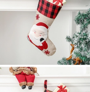 Hanging Christmas stocking with Santa Claus motif and red plaid cuff on fireplace mantel
