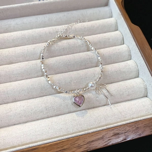 Detail of silver beaded bracelet with pink heart, white pearl, and bow charms