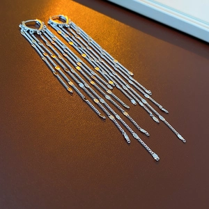 Macro shot of silver tassel earrings with heart links on dark leather background