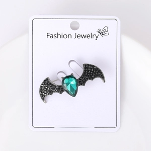 Detail of bat-shaped brooch with green teardrop crystal and black rhinestone wings