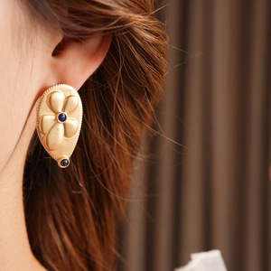 Detail view of vintage gold floral earring with blue gemstone drop on model