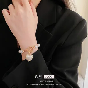 Elegante bracciale di perle con chiusura OT dorata e ciondolo a cuore al polso