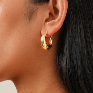 Side view detail of a chunky golden hoop earring with polished metallic surface and teardrop shape