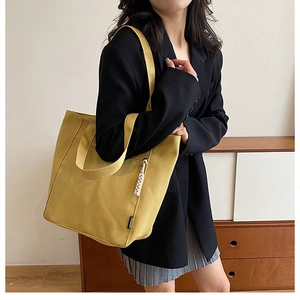 Close-up of yellow canvas tote bag with woven tassel charm and fashion label tag