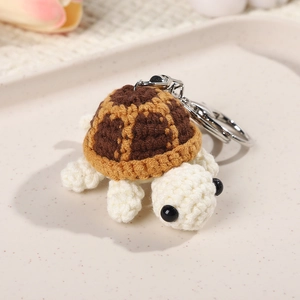 Handmade crochet turtle keychain with brown shell and silver ring on a white tray