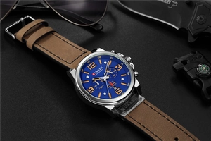 Macro detail of blue chronograph watch dial with brown leather strap and outdoor gear