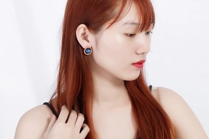 Close-up of a model wearing a deep blue crystal stud earring in a gold gear-shaped setting