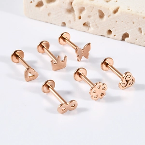 Detail of rose gold stainless steel piercings featuring crown, butterfly, and heart designs