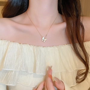 Dettaglio di una collana a farfalla placcata oro con zircone e conchiglia su una modella