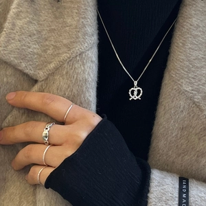 Close-up of 925 silver twist heart necklace and stacked rings on a model