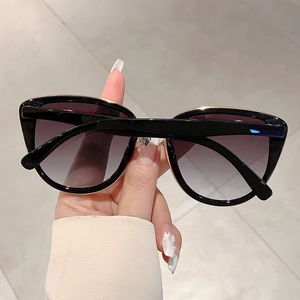 Close-up of black cat-eye sunglasses with gold metal top trim and grey gradient lenses