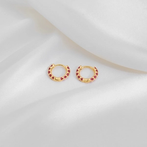 Minimalist gold hoop earrings with red polka dots displayed on white silk texture
