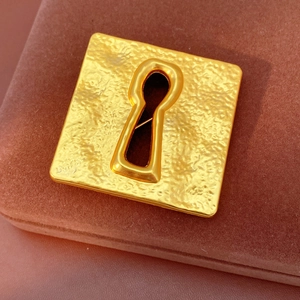 Macro shot of vintage gold square brooch featuring textured surface and keyhole detail