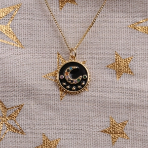 Detail of gold crescent moon pendant with black enamel and colored crystals on chain