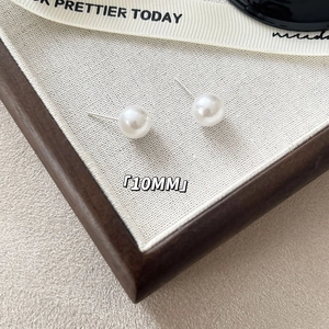 Detail view of 10mm glossy white pearl earrings with S925 silver needle on textured fabric