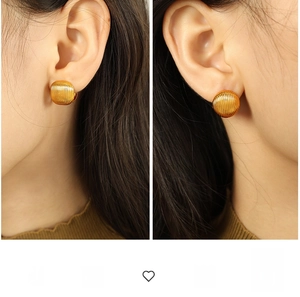 Détail de boucles d'oreilles rondes dorées à texture rayée verticale portées par le modèle