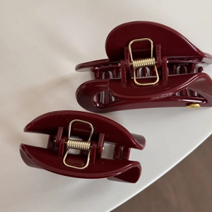 Detail view of two dark red heart-shaped hair claws with golden metal springs and accents