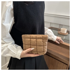 Close-up of khaki quilted down clutch bag held by model in a cozy indoor setting