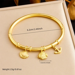 Detailed view of gold bangle with ocean charms and measurements on a beige jewelry box