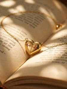 Collana con ciondolo a cuore dorato e battito rosso su un libro sotto la luce