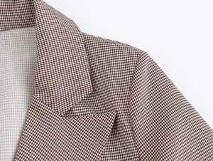 Dettaglio del classico motivo pied-de-poule su un blazer lungo marrone a doppio petto chic