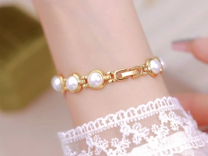 Detailed close-up of a gold pearl bracelet watch with white lace sleeve background