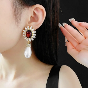 Detail of flower earring with red oval gemstone and large teardrop pearl on a model