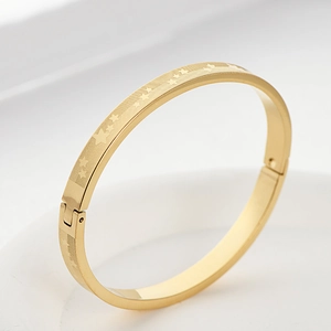 Dettaglio di un bracciale in acciaio al titanio dorato con stelle incise e texture diagonali