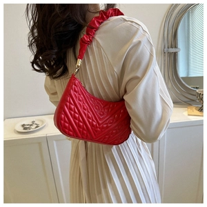 Detail of red quilted faux leather underarm bag with ruffled strap worn by model