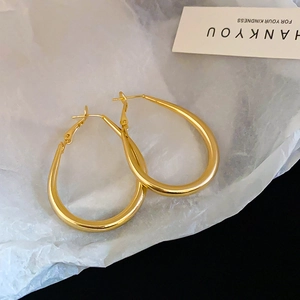 Macro detail of glossy gold oval hoop earrings on elegant textured paper background