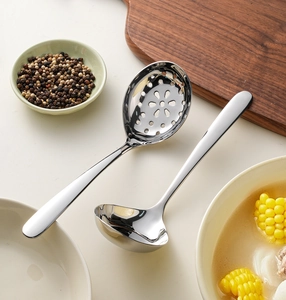 Polished stainless steel soup spoon and slotted spoon set on a kitchen table