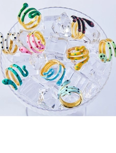 Detailed shot of multi-color enamel snake rings with gold plating displayed on ice glass