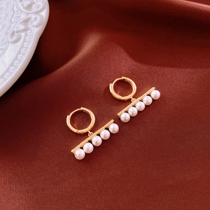 Close-up of gold geometric pearl earrings on elegant dark red silk fabric backdrop