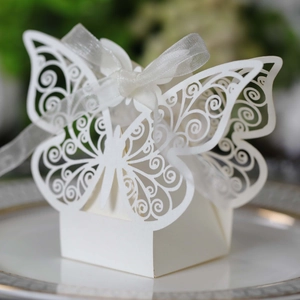 Detail of white laser-cut butterfly wedding favor box with ribbon on elegant plate