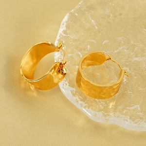 Boucles d'oreilles créoles larges dorées avec texture martelée sur fond de soie