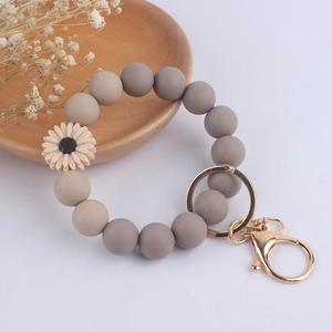Detail of gray silicone beaded keychain bracelet with a white daisy charm and gold clasp