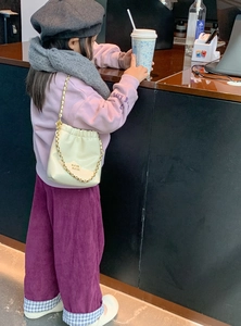 Detail einer beigen PU-Kettentasche kombiniert mit lila Kordhose in einer Café-Umgebung