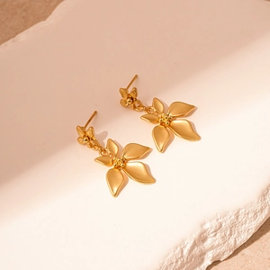 Detail of golden double-layered flower petal earrings on a white textured stone background
