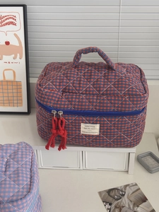 Detail of red and blue checkered quilted makeup bag with handle and blue zipper closure