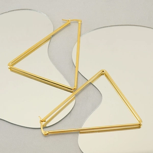 Artistic close-up of gold geometric triangle hoop earrings on a reflective mirror surface