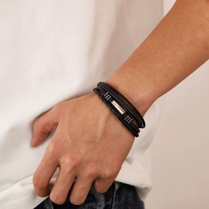 Detail of a multi-layer black leather braided bracelet with silver metal clasp on wrist