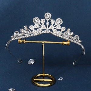 Detailed view of bridal rhinestone crown on a golden stand with blue background