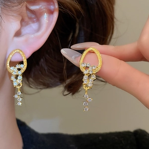 Detailed close-up showing golden fringed earrings with sparkling zircons and textured hoops