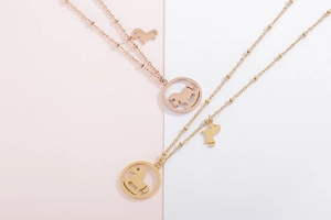 Détail de deux pendentifs cheval à bascule sur colliers or et or rose sur fond rose