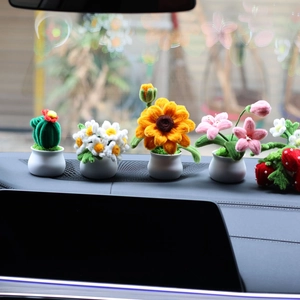 Handmade knitted sunflower and strawberry mini potted plants displayed on car dashboard