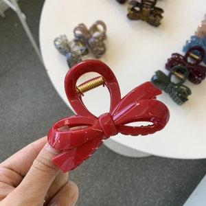 Close-up of a glossy red bow hair claw clip featuring a durable golden metal spring