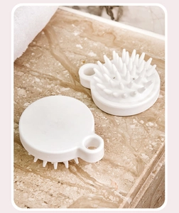 Detailed view of white silicone scalp massager and shampoo brushes on marble surface