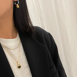 Detail of a gold necklace with black heart pendant and bicolor hoop earrings on a model