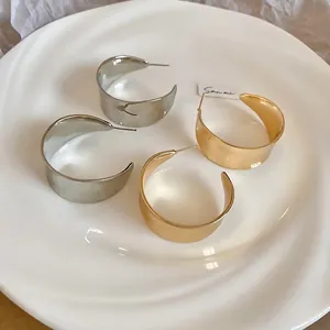 Polierte silberne und matte goldene C-Form Metallohrstecker auf einem Keramiktablett