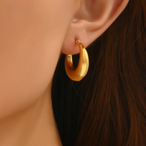 Macro close-up of chunky golden hoop earrings with a polished finish on a model